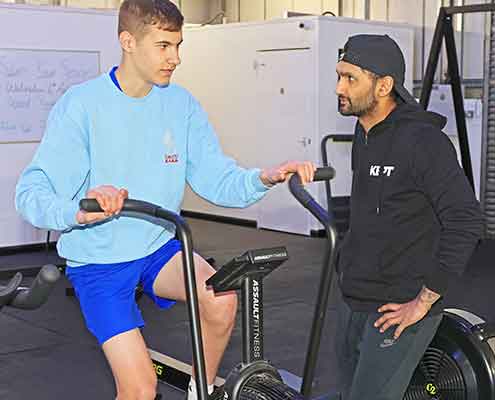 A man on an exercise bike being coached by a fitness trainer in Ashford